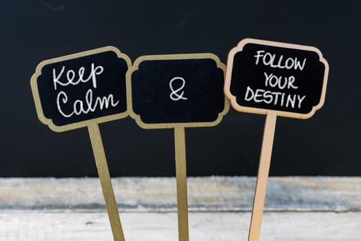 Keep Calm and Follow Your Destinity message written with chalk on mini blackboard labels, defocused chalkboard and wooden table in background. Fun and humor concept