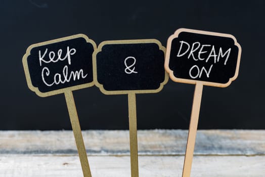 Keep Calm and Dream On message written with chalk on mini blackboard labels, defocused chalkboard and wooden table in background. Fun and humor concept