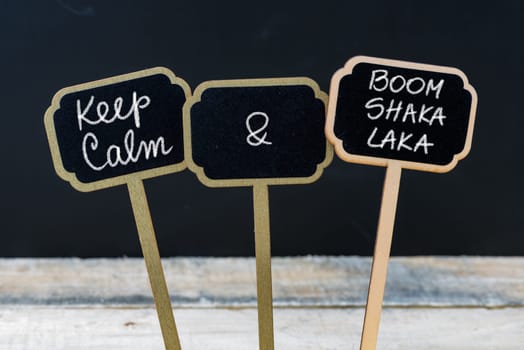 Keep Calm and Boom Shaka Laka message written with chalk on mini blackboard labels, defocused chalkboard and wooden table in background. Fun and humor concept