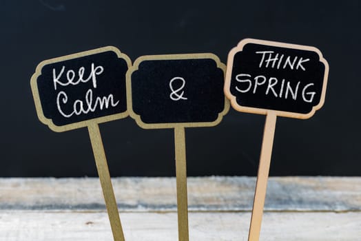 Keep Calm and Think Spring message written with chalk on mini blackboard labels, defocused chalkboard and wooden table in background. Fun and humor concept