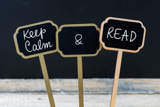 Keep Calm and Read message written with chalk on mini blackboard labels, defocused chalkboard and wooden table in background. Fun and humor concept