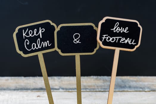 Keep Calm and Love Football message written with chalk on mini blackboard labels, defocused chalkboard and wooden table in background. Fun and humor concept
