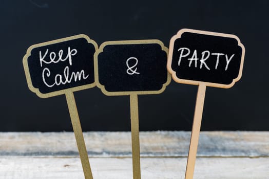 Keep Calm and Party message written with chalk on mini blackboard labels, defocused chalkboard and wooden table in background. Fun and humor concept