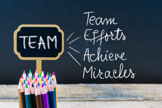 Business Acronym TEAM as Team Efforts Achieve Miracles written with chalk on wooden mini blackboard labels and chalkboard background.