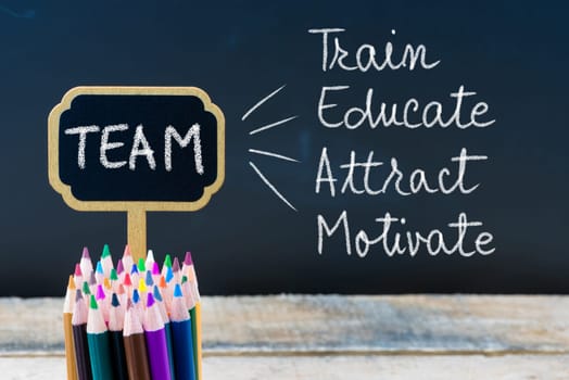 Business Acronym TEAM Train Educate Attract Motivate written with chalk on wooden mini blackboard labels and chalkboard background.
