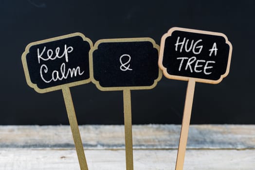 Keep Calm and Hug A Tree message written with chalk on mini blackboard labels, defocused chalkboard and wooden table in background. Fun and humor concept