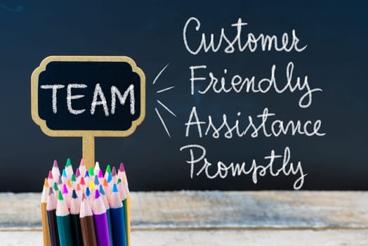 Business Acronym TEAM Customer Friendly Assistance Promptly written with chalk on wooden mini blackboard labels and chalkboard background.