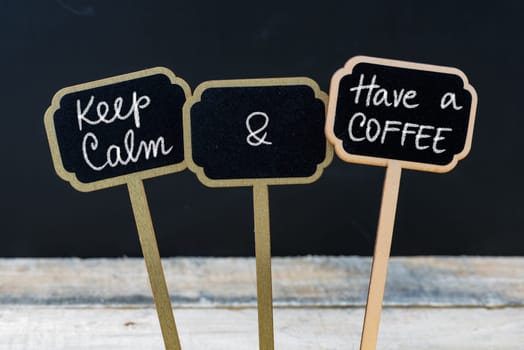 Keep Calm and Have A Coffee message written with chalk on mini blackboard labels, defocused chalkboard and wooden table in background. Fun and humor concept
