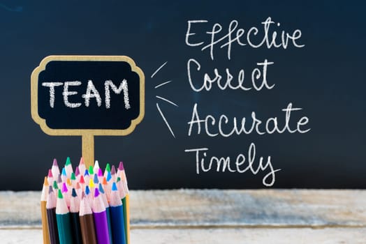Business Acronym TEAM Effective Correct Accurate Timely written with chalk on wooden mini blackboard labels and chalkboard background.
