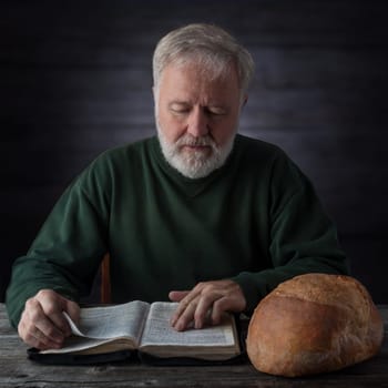 Senior pastor meditating and feeding on the Word of God not only with the daily bread next to him. Mat.4.4 Man shall not live by bread alone, but by every word that proceedeth out of the mouth of God