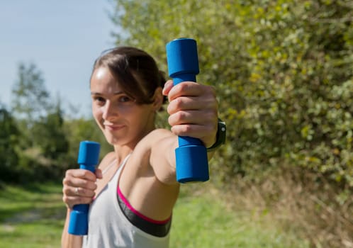 Fitness woman doing exercises with blue dumbbells in the countryside