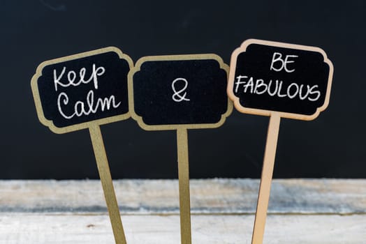 Keep Calm and Be Fabulous message written with chalk on mini blackboard labels, defocused chalkboard and wooden table in background. Fun and humor concept