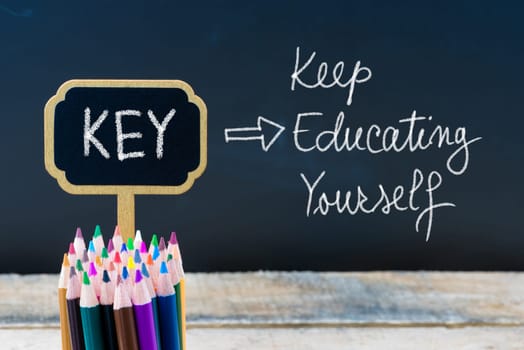 Business Acronym KEY Keep Educating Yourself written with chalk on wooden mini blackboard labels and chalkboard background.