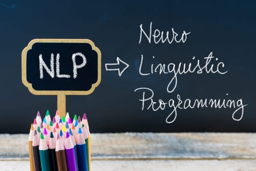 Business Acronym NLP Neuro Linguistic Programming written with chalk on wooden mini blackboard labels and chalkboard background.