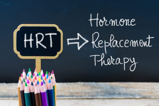 Business Acronym HRT Hormone Replacement Therapy written with chalk on wooden mini blackboard labels and chalkboard background.