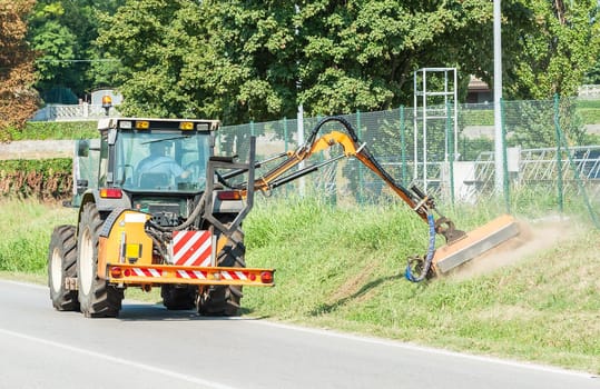Road maintenance. Mowing grass on the roadside with tractor.