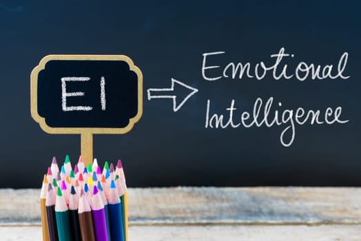 Business Acronym EI Emotional Intelligence written with chalk on wooden mini blackboard labels and chalkboard background.
