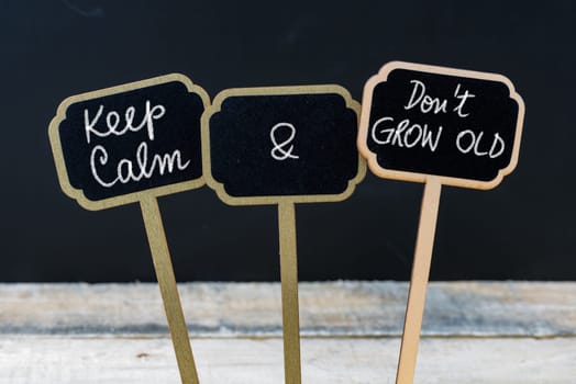 Keep Calm and Do Not Grow Old message written with chalk on mini blackboard labels, defocused chalkboard and wooden table in background. Fun and humor concept