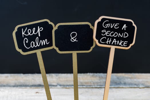 Keep Calm and Give A Second Chance message written with chalk on mini blackboard labels, defocused chalkboard and wooden table in background. Fun and humor concept
