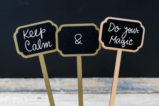 Keep Calm and Do Your Magic message written with chalk on mini blackboard labels, defocused chalkboard and wooden table in background. Fun and humor concept
