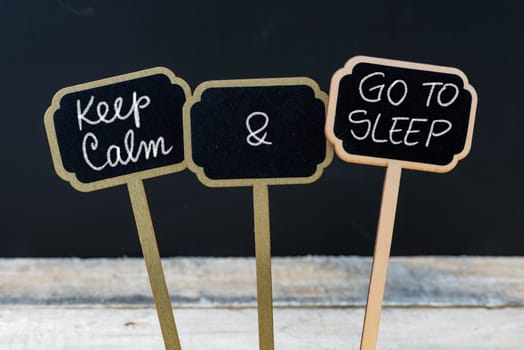 Keep Calm and Go To Sleep message written with chalk on mini blackboard labels, defocused chalkboard and wooden table in background. Fun and humor concept