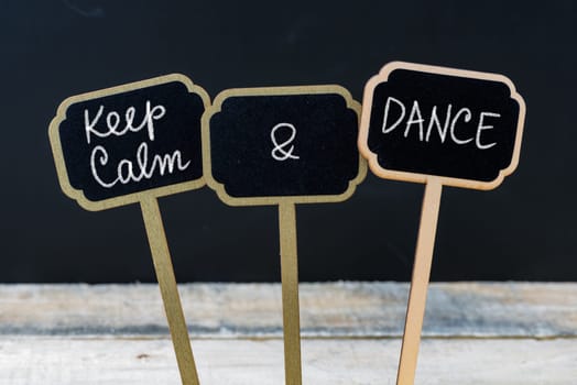 Keep Calm and Dance message written with chalk on mini blackboard labels, defocused chalkboard and wooden table in background. Fun and humor concept