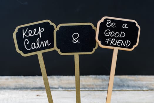Keep Calm and Be A Good Friend message written with chalk on mini blackboard labels, defocused chalkboard and wooden table in background. Fun and humor concept