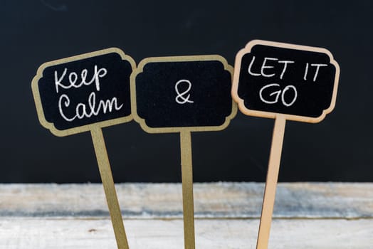 Keep Calm and Let It Go message written with chalk on mini blackboard labels, defocused chalkboard and wooden table in background. Fun and humor concept