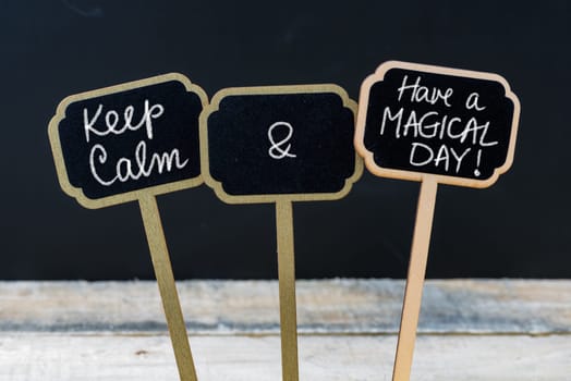 Keep Calm and Have A Magical Day message written with chalk on mini blackboard labels, defocused chalkboard and wooden table in background. Fun and humor concept