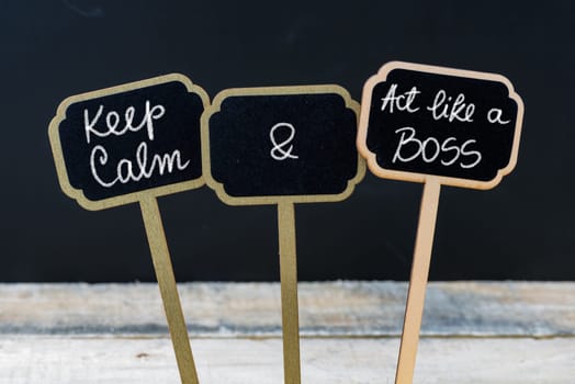 Keep Calm and Act Like A Boss message written with chalk on mini blackboard labels, defocused chalkboard and wooden table in background. Fun and humor concept