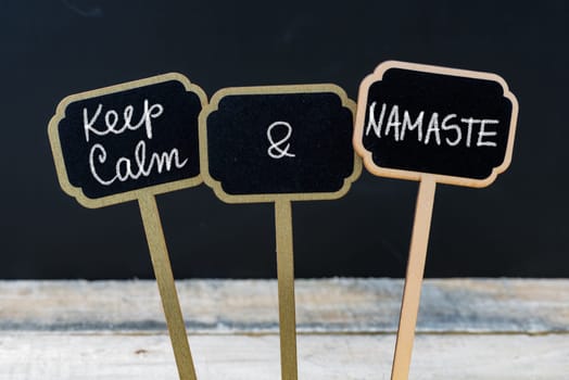 Keep Calm and Namaste message written with chalk on mini blackboard labels, defocused chalkboard and wooden table in background. Fun and humor concept