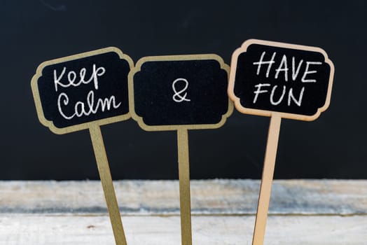 Keep Calm and Have Fun message written with chalk on mini blackboard labels, defocused chalkboard and wooden table in background. Fun and humor concept
