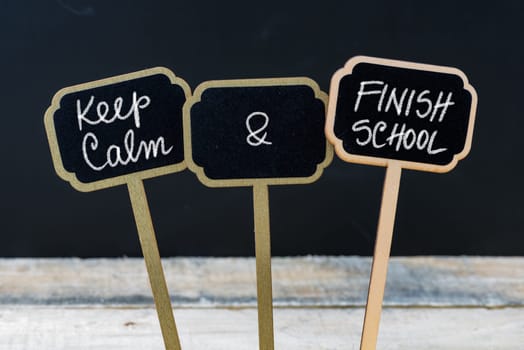 Keep Calm and Finish School message written with chalk on mini blackboard labels, defocused chalkboard and wooden table in background. Fun and humor concept