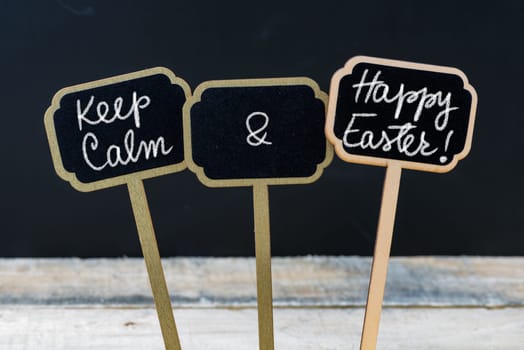 Keep Calm and Happy Easter message written with chalk on mini blackboard labels, defocused chalkboard and wooden table in background. Fun and humor concept