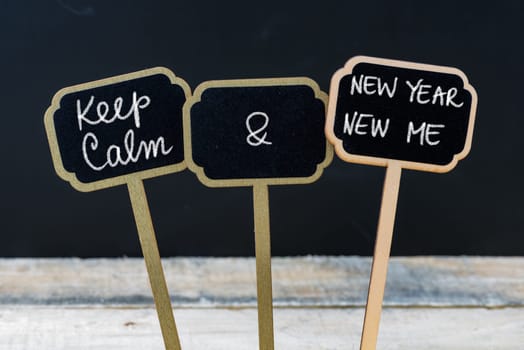 Keep Calm and New Year New Me message written with chalk on mini blackboard labels, defocused chalkboard and wooden table in background. Fun and humor concept