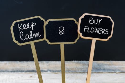 Keep Calm and Buy Flowers message written with chalk on mini blackboard labels, defocused chalkboard and wooden table in background. Fun and humor concept