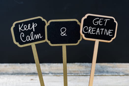 Keep Calm and Get Creative message written with chalk on mini blackboard labels, defocused chalkboard and wooden table in background. Fun and humor concept
