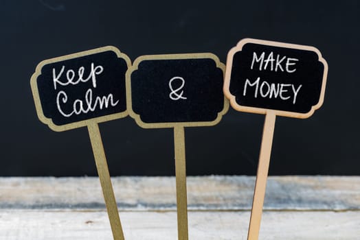 Keep Calm and Make Money message written with chalk on mini blackboard labels, defocused chalkboard and wooden table in background. Fun and humor concept