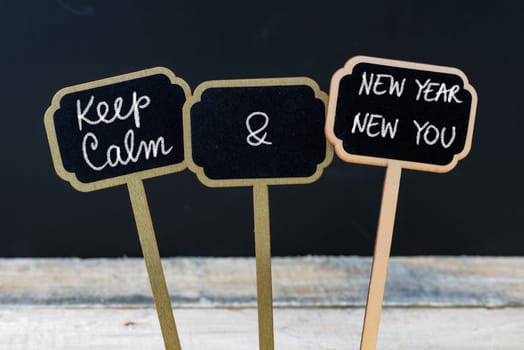 Keep Calm and New Year New You message written with chalk on mini blackboard labels, defocused chalkboard and wooden table in background. Fun and humor concept