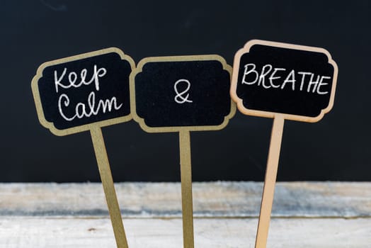 Keep Calm and Breathe message written with chalk on mini blackboard labels, defocused chalkboard and wooden table in background. Fun and humor concept
