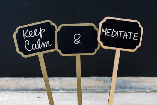 Keep Calm and Meditate message written with chalk on mini blackboard labels, defocused chalkboard and wooden table in background. Fun and humor concept