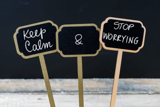 Keep Calm and Stop Worrying message written with chalk on mini blackboard labels, defocused chalkboard and wooden table in background. Fun and humor concept