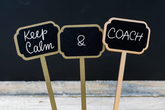 Keep Calm and Coach message written with chalk on mini blackboard labels, defocused chalkboard and wooden table in background. Fun and humor concept