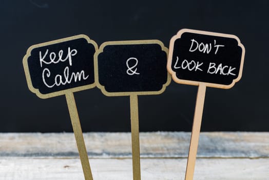 Keep Calm and Do Not Look Back message written with chalk on mini blackboard labels, defocused chalkboard and wooden table in background. Fun and humor concept