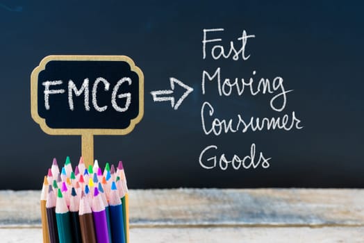 Business Acronym FMCG Fast Moving Consumer Goods written with chalk on wooden mini blackboard labels and chalkboard background.