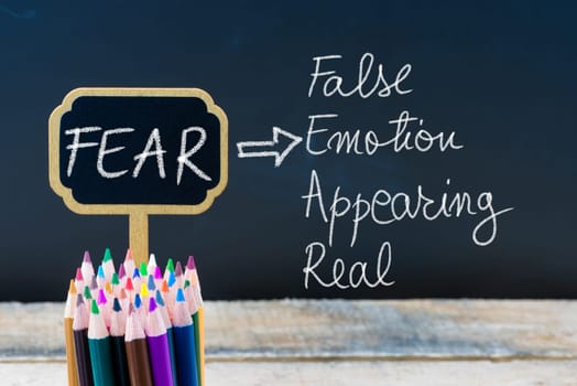 Business Acronym FEAR False Emotion Appearing Real written with chalk on wooden mini blackboard labels and chalkboard background.