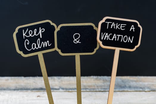 Keep Calm and Take A Vacation message written with chalk on mini blackboard labels, defocused chalkboard and wooden table in background. Fun and humor concept