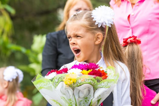 First grader with a bouquet of flowers yawns at school in a crowd