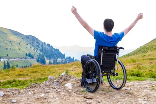 Young man in a wheelchair enjoying fresh air in a sunny day on the mountain.