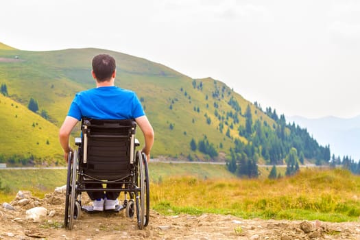 Young man in a wheelchair enjoying fresh air in a sunny day on the mountain.